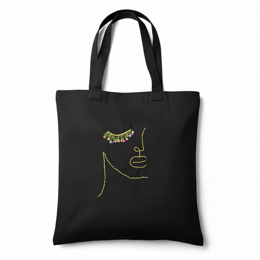 Black tote bag with artistic face design on white background