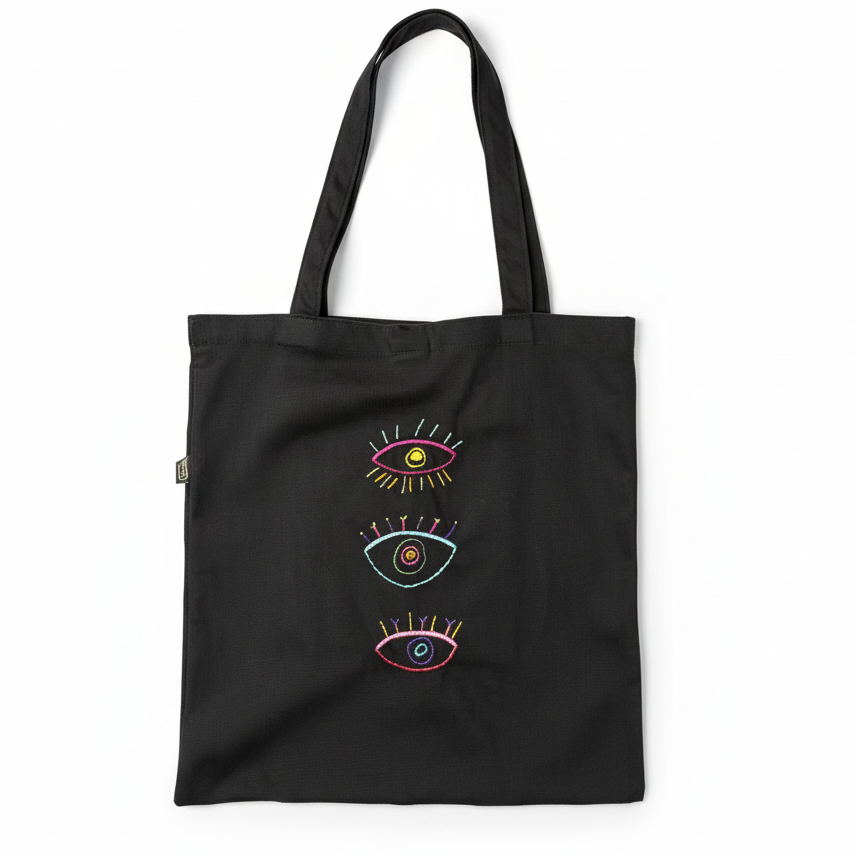 Black tote bag with three embroidered eyes on white background