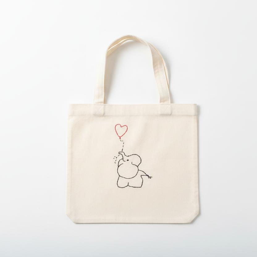 Cream white canvas tote bag with embroidered baby elephant and heart balloon on white background