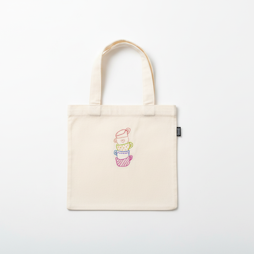 Cream white canvas tote bag with embroidered stacked teacups on white background